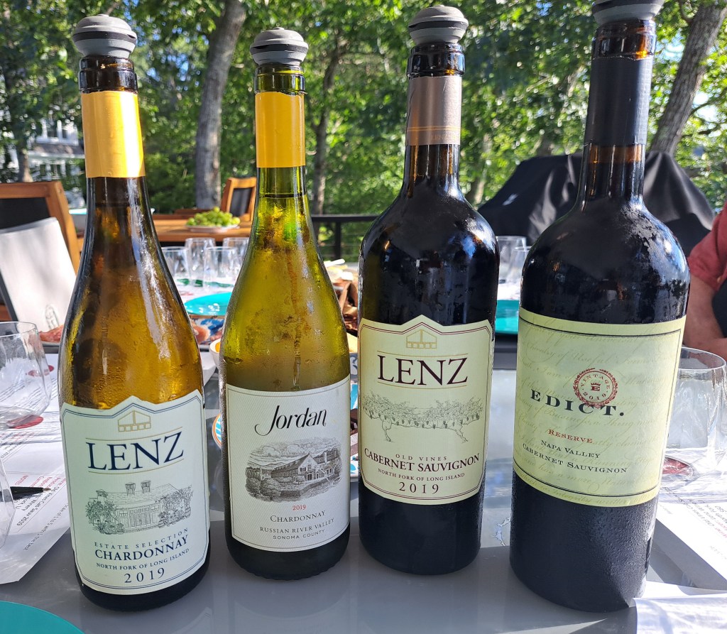 Four wine bottles displayed on a table, including Lenz Chardonnay, Jordan Chardonnay, Lenz Cabernet Sauvignon, and Edict Cabernet Sauvignon, with a green natural background.